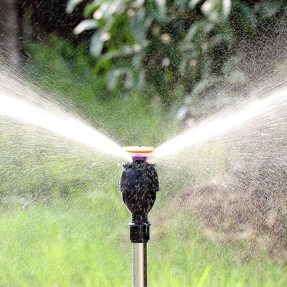 Adjustable garden sprinkler with tripod in use on lawn showing full-circle rotating spray pattern